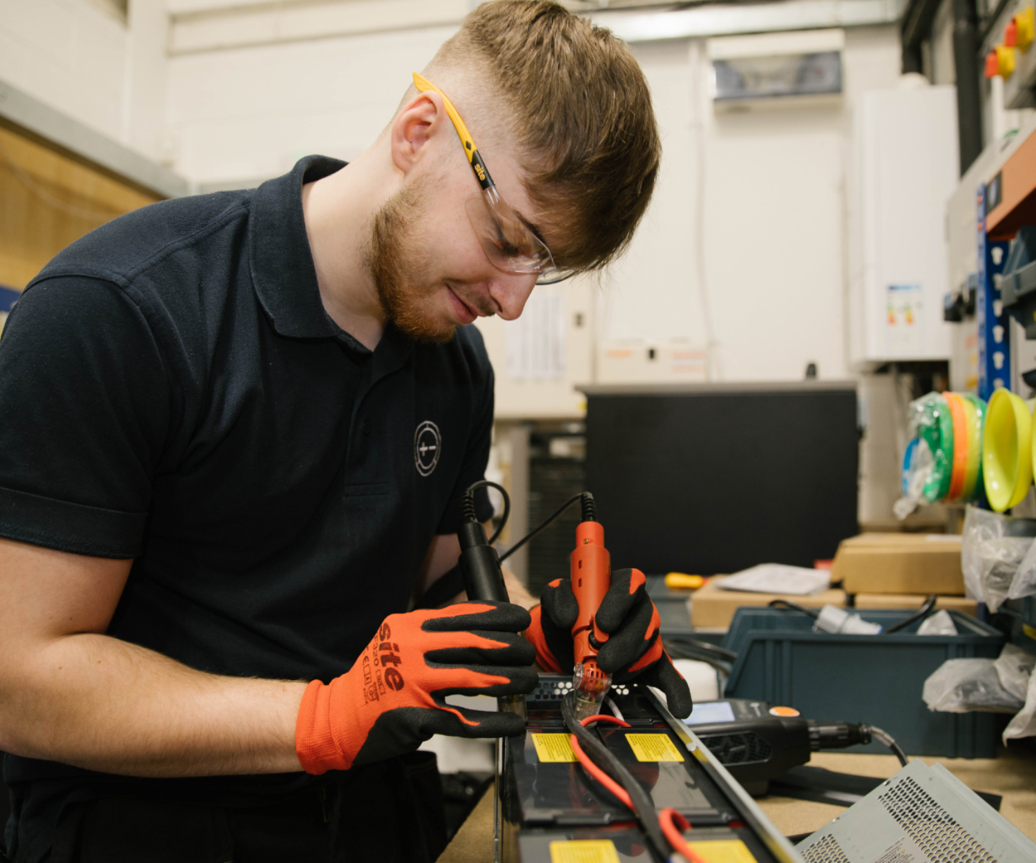 Man smiles whilst working on battery wearing orange gloves